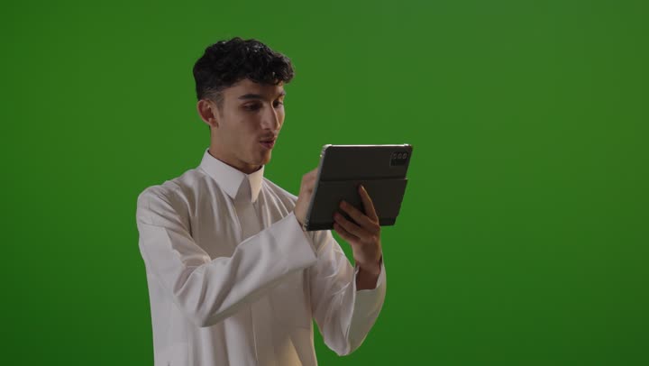 شاب سعودي يستخدم جهاز لوحي أمام خلفية خضراء