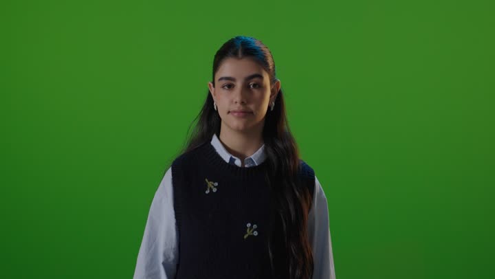 لقطة استوديو لطالبة مدرسة تبتسم أمام خلفية خضراء