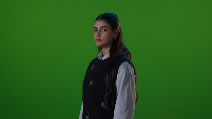 طالبة مدرسة أمام خلفية خضراء تبتسم بوضعية مكتوفة الأيدي