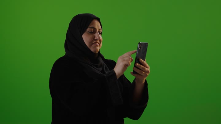 امرأة عربية تستخدم الهاتف الذكي أمام شاشة خضراء