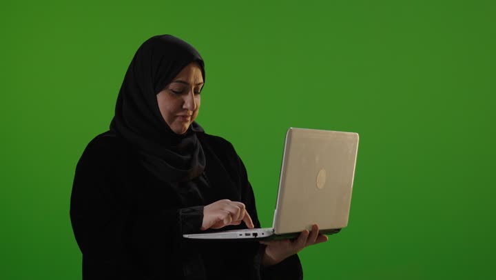 امرأة سعودية تستخدم الكمبيوتر المحمول أمام كروما خضراء
