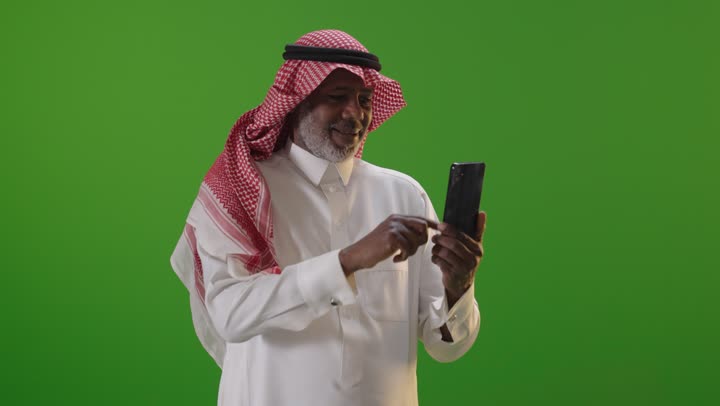 رجل سعودي مسن يستخدم هاتف ذكي أمام كروما خضراء