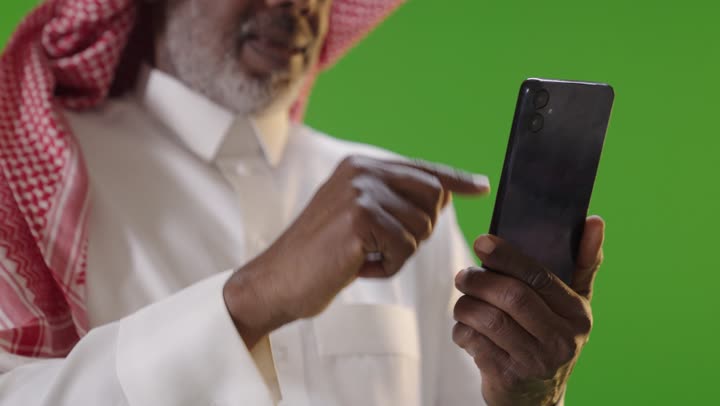 رجل عربي مسن يستخدم الهاتف الذكي أمام خلفية خضراء