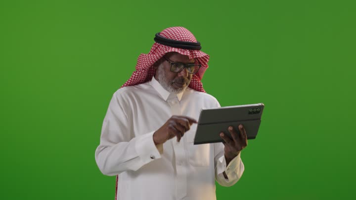 رجل سعودي يستخدم جهاز لوحي على شاشة خضراء