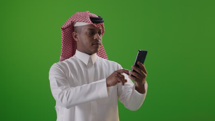 رجل سعودي يستخدم الهاتف الذكي أمام خلفية خضراء