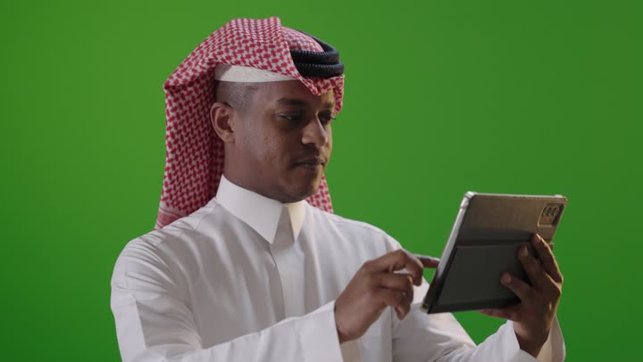 رجل سعودي يستخدم جهاز لوحي على خلفية خضراء