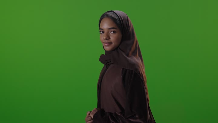 امرأة سعودية بالعباءة تبتسم أمام شاشة خضراء