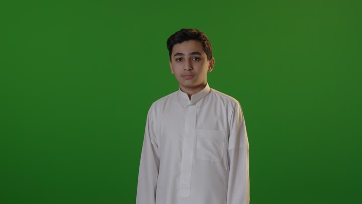 فتى سعودي بالثوب يبتسم على خلفية خضراء