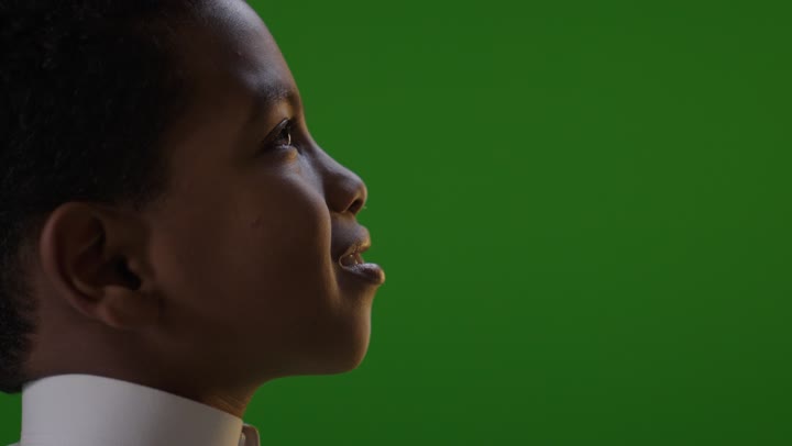 طفل سعودي يرتدي الثوب الأبيض التقليدي ينظر للأعلى أثناء وقوفه أمام خلفية الكروما الخضراء. يلتفت الطفل برأسه نحو الكاميرا مبتسماً في لقطة جانبية داخل استوديو تصوير.