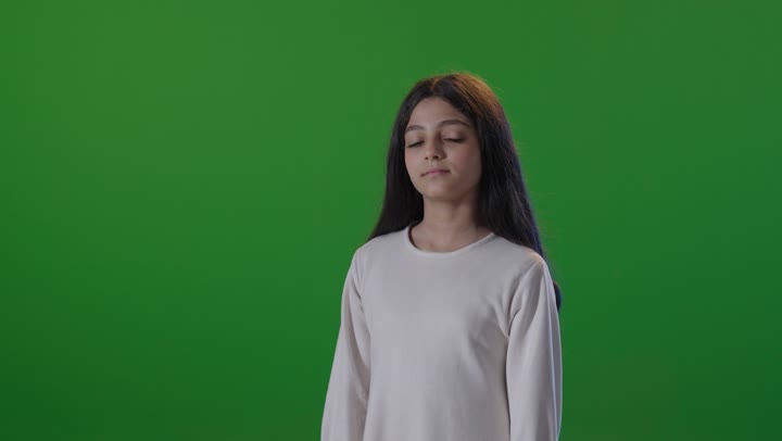 A Saudi Arabian Gulf girl wearing casual attire is looking at the camera with her arms crossed and smiling, with a green chroma background.