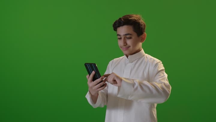صبي سعودي يستخدم الهاتف الذكي على خلفية خضراء