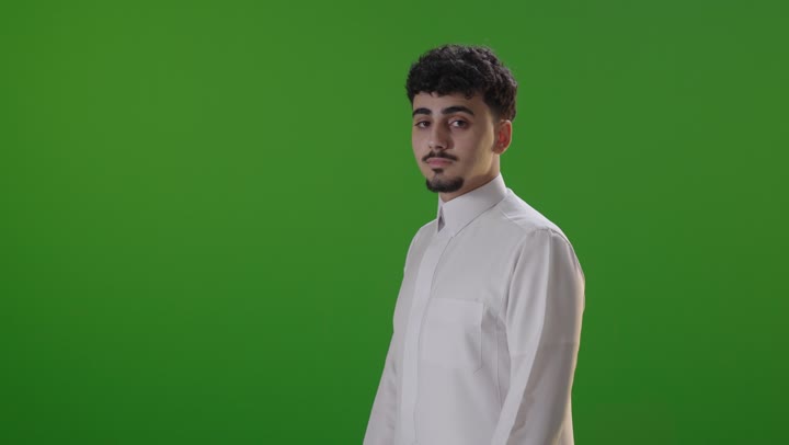 شاب سعودي بالثوب التقليدي يبتسم أمام خلفية خضراء