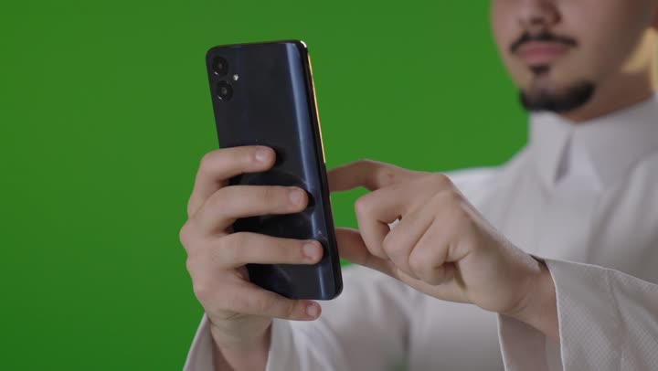 رجل سعودي يستخدم الهاتف الذكي أمام الكروما
