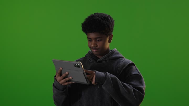 فتى سعودي يستخدم جهازاً لوحياً أمام خلفية خضراء