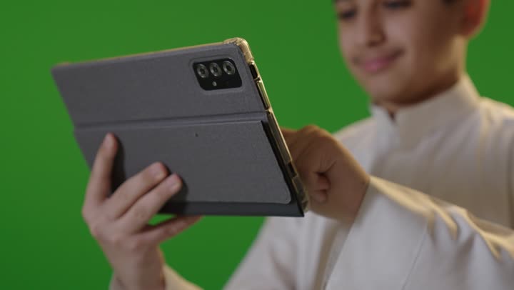 فتى سعودي يستخدم جهازاً لوحياً أمام خلفية كروما خضراء