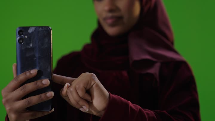 امرأة سعودية تستخدم هاتف ذكي أمام شاشة خضراء