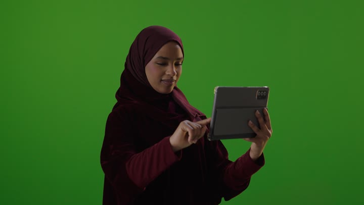 امرأة سعودية تستخدم جهازاً لوحياً أمام خلفية كروما خضراء