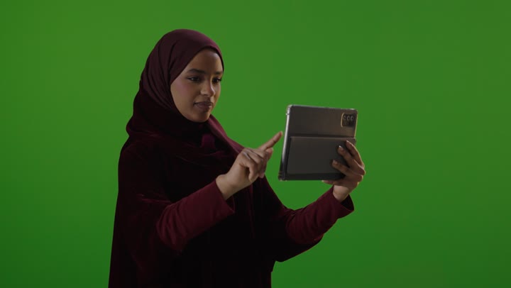 امرأة سعودية تستخدم جهاز لوحي أمام خلفية خضراء