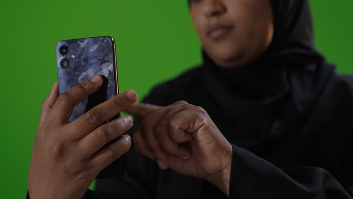 امرأة سعودية تستخدم هاتف ذكي على خلفية كروما خضراء