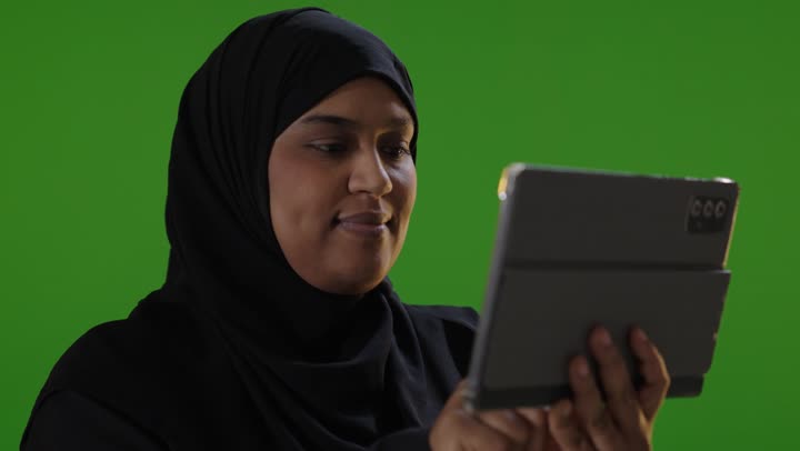 امرأة سعودية تستخدم جهاز لوحي أمام خلفية خضراء