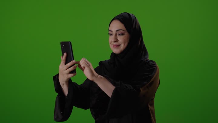 امرأة سعودية تستخدم الهاتف الذكي أمام كروما خضراء