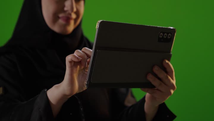 امرأة سعودية تستخدم جهاز لوحي رقمي على خلفية خضراء