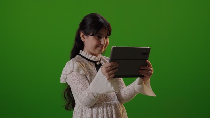 طفلة سعودية تستخدم جهاز لوحي أمام خلفية خضراء