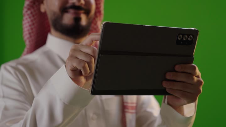 رجل سعودي يستخدم جهاز لوحي أمام خلفية خضراء