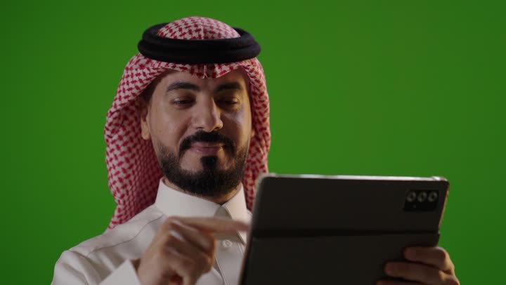 رجل سعودي يستخدم جهاز لوحي أمام شاشة خضراء كروما