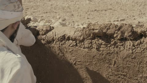 رجل يبني جداراً طينياً تقليدياً في الصحراء