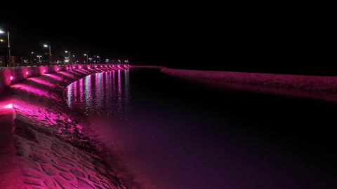 Pink night lighting and reflections on the coastal walkway in the city of Yanbu.