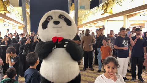 Panda Mascot Interacting with Crowd in Night Marketplace