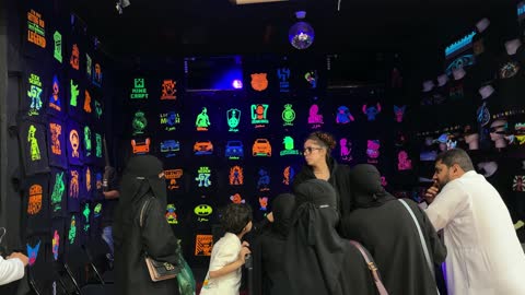 عائلة سعودية تتسوق في متجر قمصان نيون ليلي