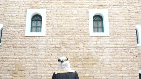 رجل سعودي بالبشت التقليدي أمام جدار تراثي بالرياض