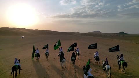 فرسان يحملون أعلام السعودية في صحراء الرياض وقت الغروب