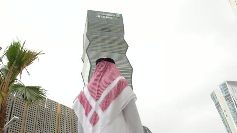رجل سعودي يمشي أمام مبنى أرامكو في لقطة حضرية عصرية