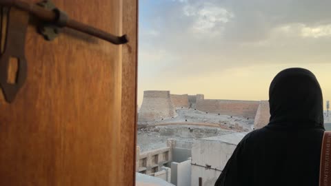امرأة بالعباءة السوداء تنظر إلى قلعة قديمة وقت الغروب