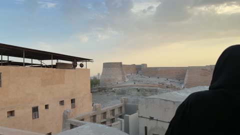 Woman in Abaya Viewing Historic Stone Fort at Sunset