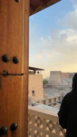 شخص ينظر من شرفة إلى حصن حجري قديم وقت الغروب