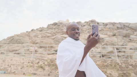 معتمر أفريقي بملابس الإحرام يستخدم الهاتف الذكي في الخارج