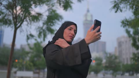 امرأة عربية تستخدم الهاتف الذكي في حديقة المدينة