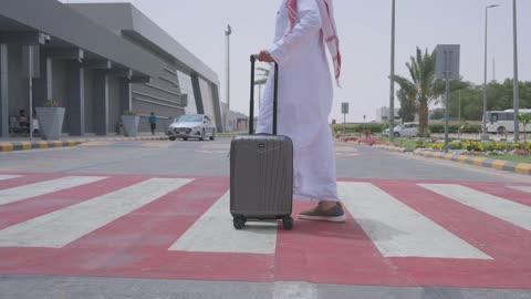 رجل سعودي يمشي بحقيبة سفر عند مدخل المطار