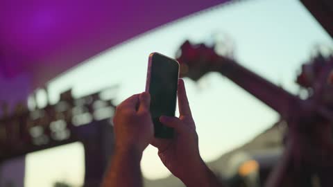 Man Filming Amusement Park with Smartphone at Night
