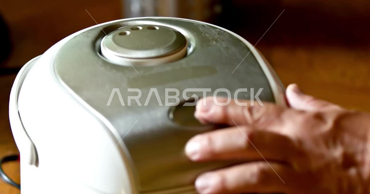 Closeup of the hand of a man using an electric steamer to cook rice