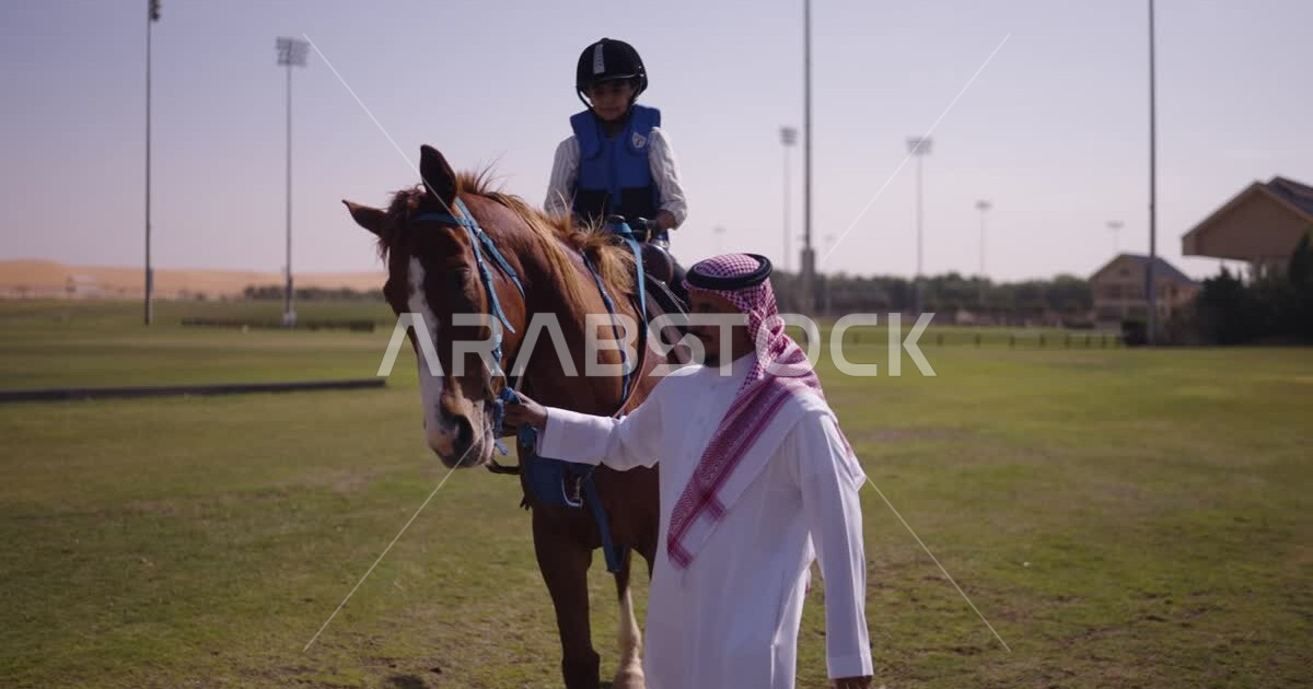 A Saudi Arabian Gulf boy rides a horse next to him, a Saudi Arabian